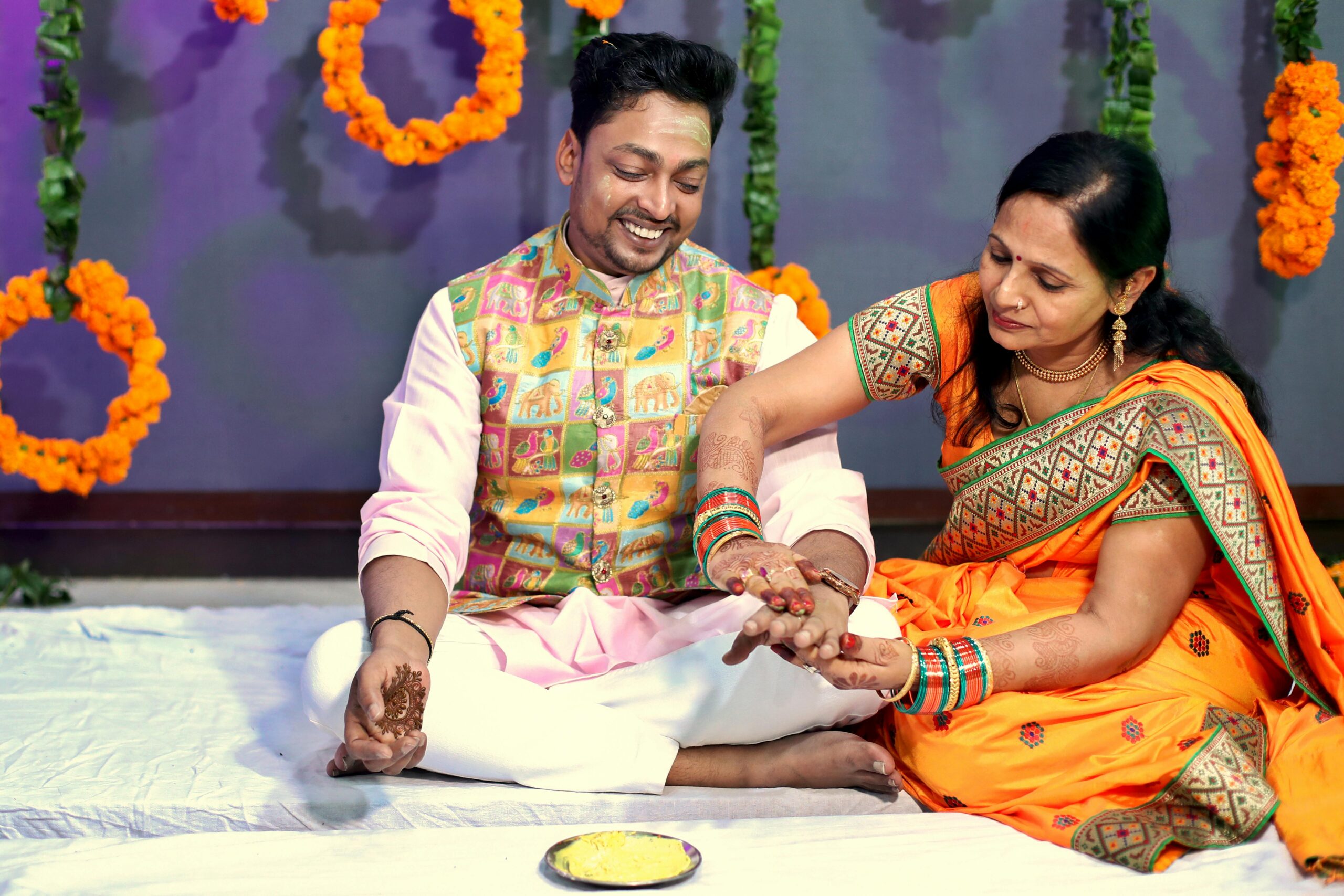 South Asian couple participate in a colorful wedding ritual with mehndi and vibrant attire.